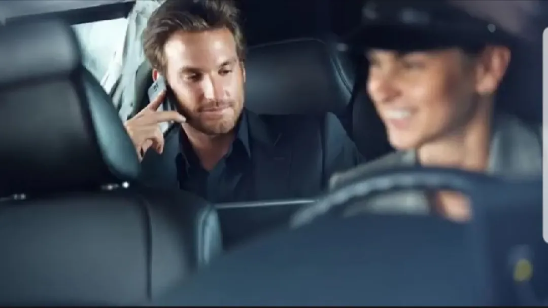 A chauffeur driving while a passenger uses a tablet in the back seat
