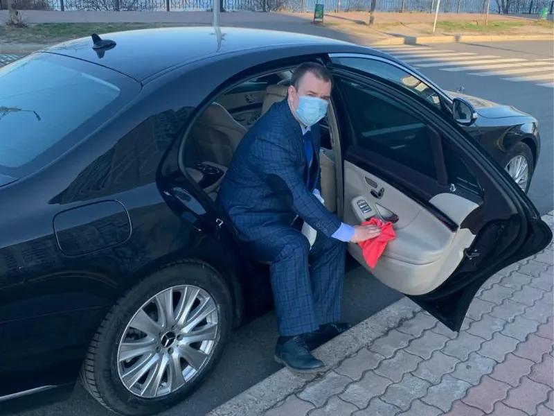 A chauffeur polishing the door of a black Mercedes