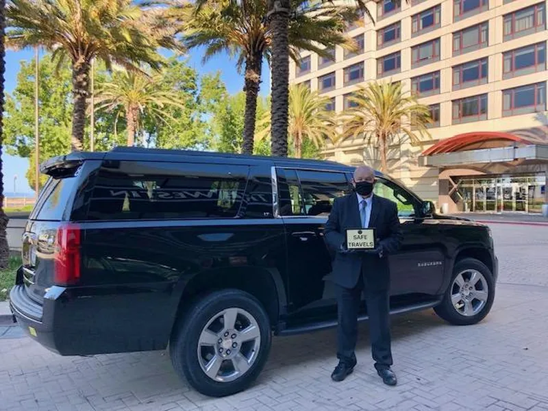 A chauffeur holding a blank name sign beside a black Escalade outside a hotel