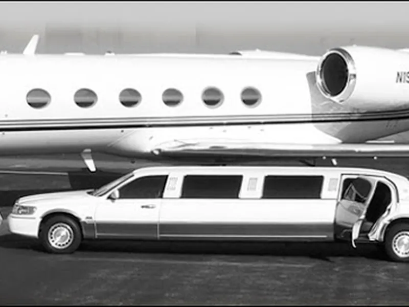 A white stretch limousine parked beside a private jet