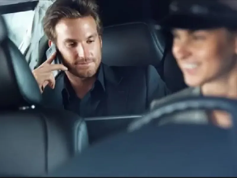 A chauffeur driving while a passenger uses a tablet in the back seat